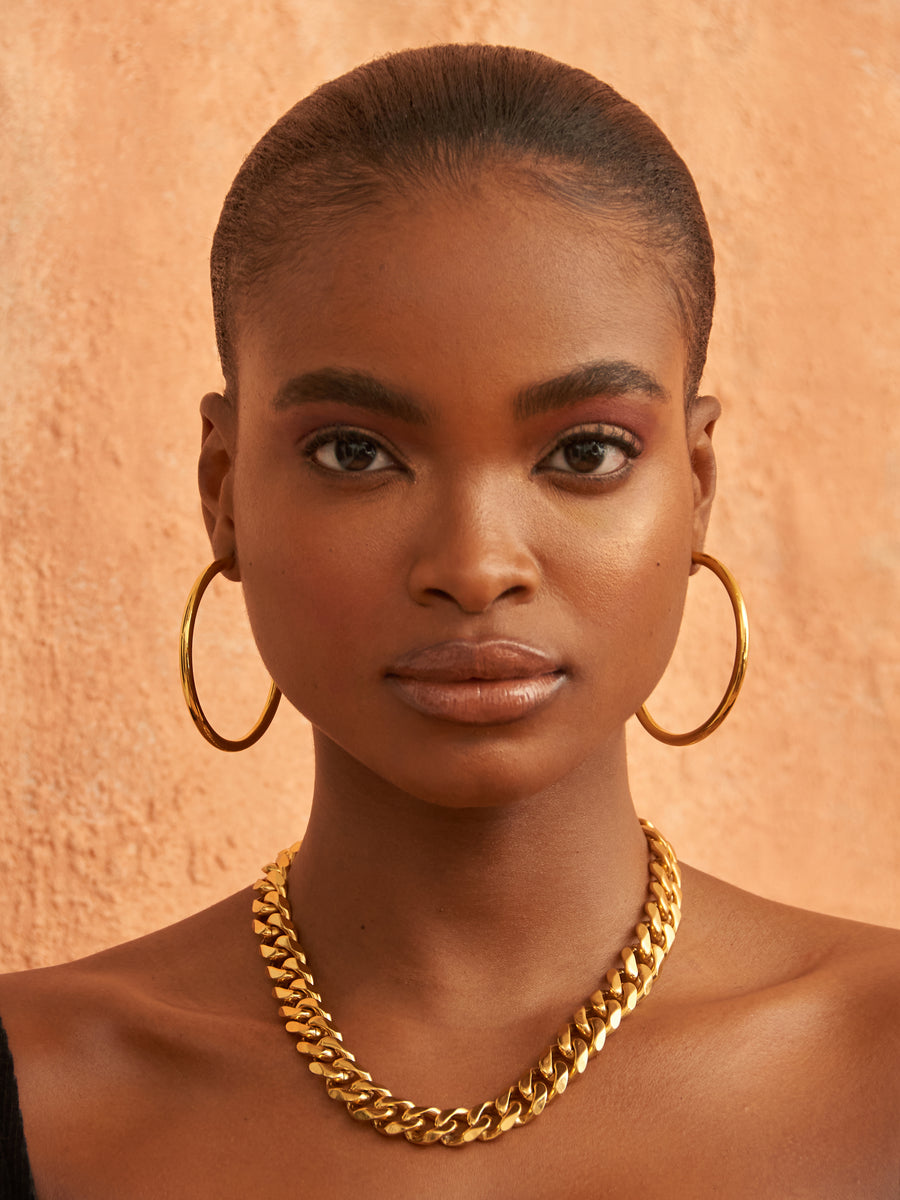 Model wearing bold gold hoops and a curb chain necklace